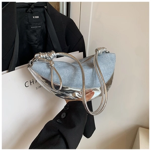 Detailed close-up of light blue denim crescent bag with silver metallic leather and knot strap