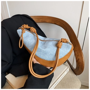 Detail of a crescent-shaped denim and leather handbag with a stylish knot shoulder strap