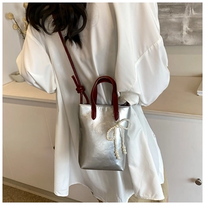 Détail d'un mini sac seau argenté avec poignée rouge foncé et breloque perle nœud