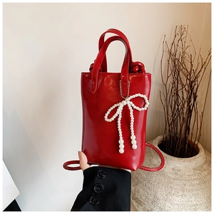Mini sac à main rouge brillant avec nœud en perles et bandoulière sur fond beige