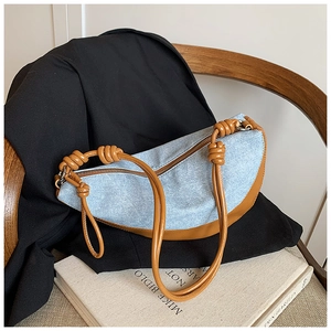 Detail of light blue denim crescent bag with brown leather trim and knot strap