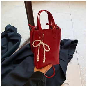 Détail du mini sac à main rouge brillant avec un charmant pendentif nœud en perles élégant