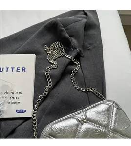 Detail of silver quilted handbag with metal butterfly logo and stylish chain strap