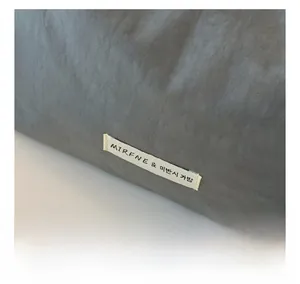 Close-up of grey woven fabric texture with MIRFNE brand label on minimalist shoulder bag