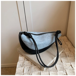 Detail of blue denim and black leather crescent bag with stylish knot strap detail