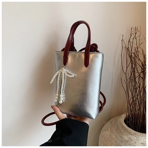 Vue détaillée du mini sac bandoulière argenté avec lanières rouges et breloque perle