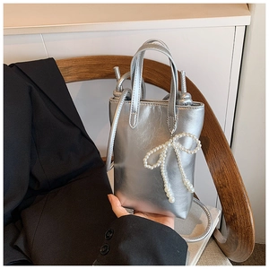 Mini sac cabas argenté avec pendentif nœud en perles sur un fauteuil élégant