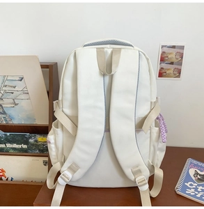 Detail of white backpack with adjustable beige straps and purple charm on a wooden desk
