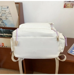 Detail view of white canvas backpack featuring purple drawstrings on a desk scene