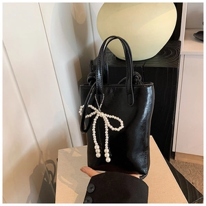 Détail d'un petit sac à main en cuir PU noir brillant avec un pendentif nœud perlé