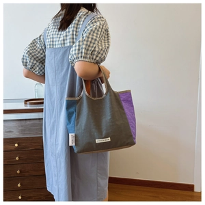 Detail of color-block canvas tote bag with gray blue and purple panels and brand label