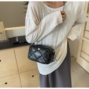 Detail of black quilted shoulder bag with silver butterfly logo and rabbit charm accessory