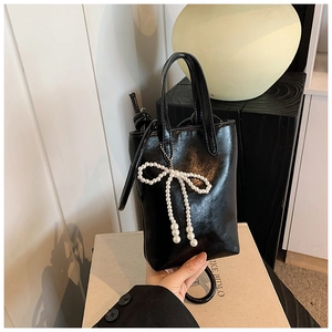 Détail d'un mini sac à main noir brillant avec un charmant nœud décoratif en perles