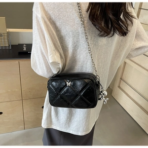 Detail of black quilted chain bag with silver butterfly and balloon dog charm