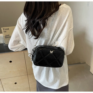 Detail of black quilted chain bag with silver butterfly charm and doll pendant on model