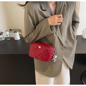 Close-up of red quilted shoulder bag with silver butterfly detail and chain strap