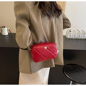 Close-up of red quilted crossbody bag with silver butterfly metal ornament and chain strap