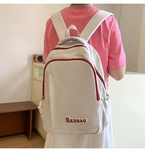 Detail of cream backpack featuring RKDBAG patch and contrasting red zipper accents