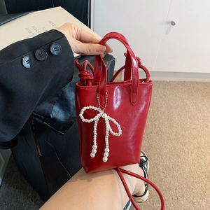 Mini sac rouge bandoulière avec nœud en perles tenu à la main pour perspective