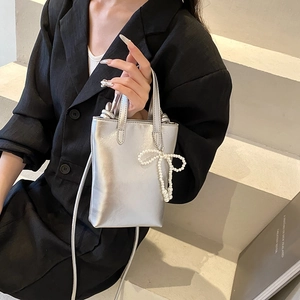 Mini sac argenté métallisé avec nœud en perles porté par un mannequin, style minimaliste