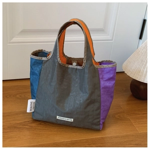 Detail of color-block tote bag with pleated texture and orange straps on a wooden table
