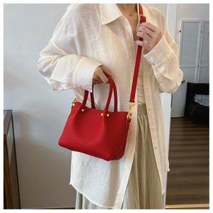 Detail of red lychee grain leather bucket bag with gold hardware on a white shirt