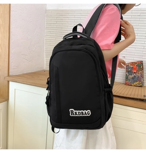 Side view of black nylon backpack with RKDBAG patch on a model against white brick