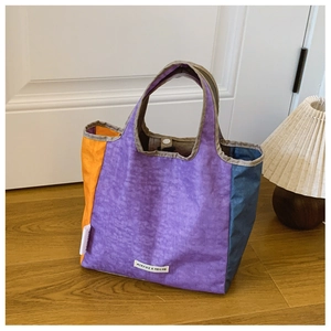 Detail of color-block canvas tote bag with snap button closure on wooden floor