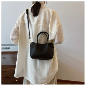 Detail of black lychee grain leather bucket bag with gold hardware on a model
