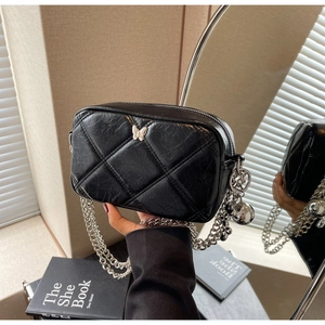 Close-up of quilted black leather bag with silver butterfly charm and metal chain strap