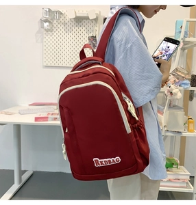 Detail view of burgundy backpack with white trim and RKDBAG logo on side shoulder