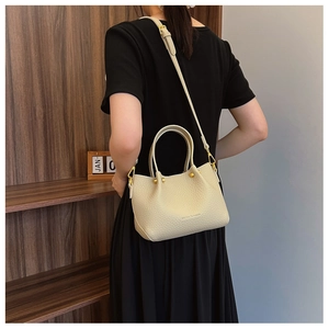 Detail of cream pebbled leather bucket bag with top handle and gold metal hardware