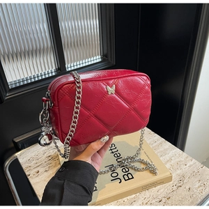 Detail of red quilted crossbody bag with silver butterfly charm and chain strap