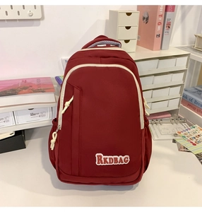 Detail view of burgundy nylon backpack featuring contrasting white zippers and logo label
