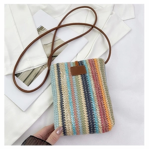 Close-up of a colorful woven straw crossbody bag with brown leather strap and patch