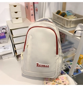 Detail view of cream backpack with red zipper accents and brand patch in a cozy setting