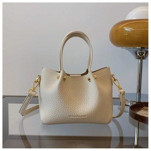 Close-up of beige pebble leather handbag with metal rivets and detachable strap detail