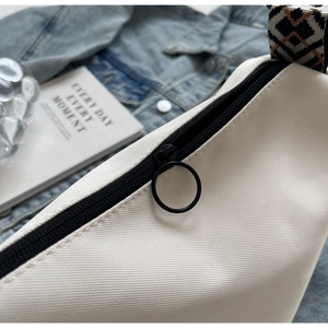 Detailed macro of white canvas bag featuring black zipper and woven geometric strap