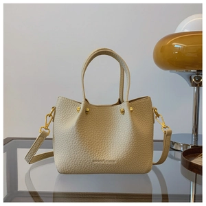 Detail of beige lychee leather texture with gold hardware on a stylish bucket bag