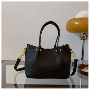 Close-up of black lychee grain leather bucket bag with gold hardware and strap