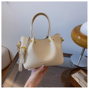 Detail of cream lychee-textured leather bucket bag with gold studs and logo embossing