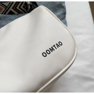 Close-up of white crossbody bag with black typography and geometric pattern strap