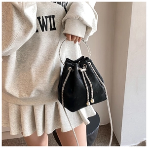 Detail of black matte bucket bag with silver metal handle and white pearl drawstring charms