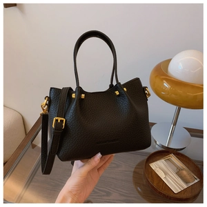 Detail of black lychee-grain bucket bag with golden metal hardware and branding