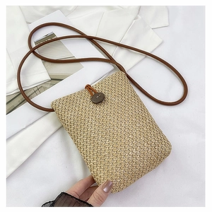 Close-up of woven straw crossbody bag with brown leather strap and wooden button