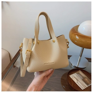 Detail of beige litchi grain leather texture and gold hardware on a bucket bag