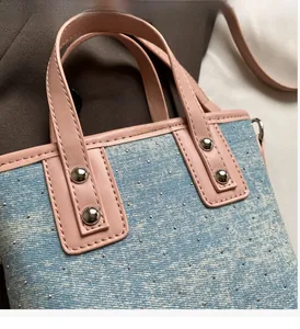 Detail of pink leather handles and silver studs on a blue denim contrast bucket bag