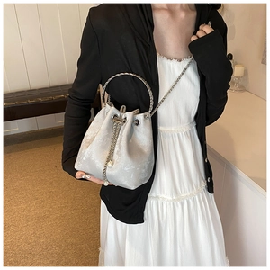 Silver bucket bag featuring metallic round handles, chain strap and pearl drawstring detail