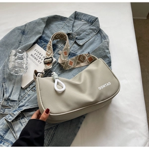 Close-up of beige crossbody bag with wide geometric strap on denim jacket