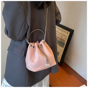 Pink velvet bucket bag with silver handle and pearl drawstrings worn over a gray blazer